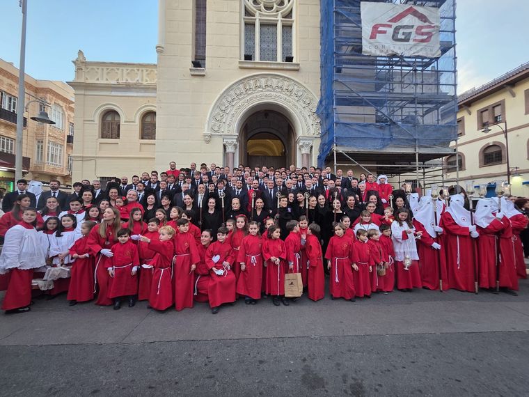 La cofradía entera posando ante la fachada de la parroquia: junta, mantillas, nazarenos y niños de túnica roja