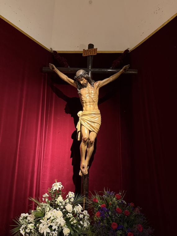 El Santísimo Cristo de la Paz crucificado sobre cortinaje granate, con flores a sus pies