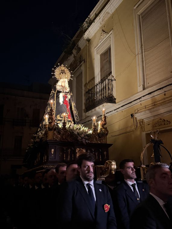 Hombres de traje oscuro portando a hombros el trono de la Virgen de la Soledad