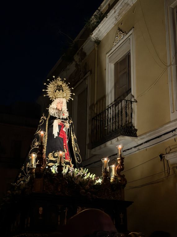 El trono de la Virgen junto a una fachada amarilla iluminada, de noche