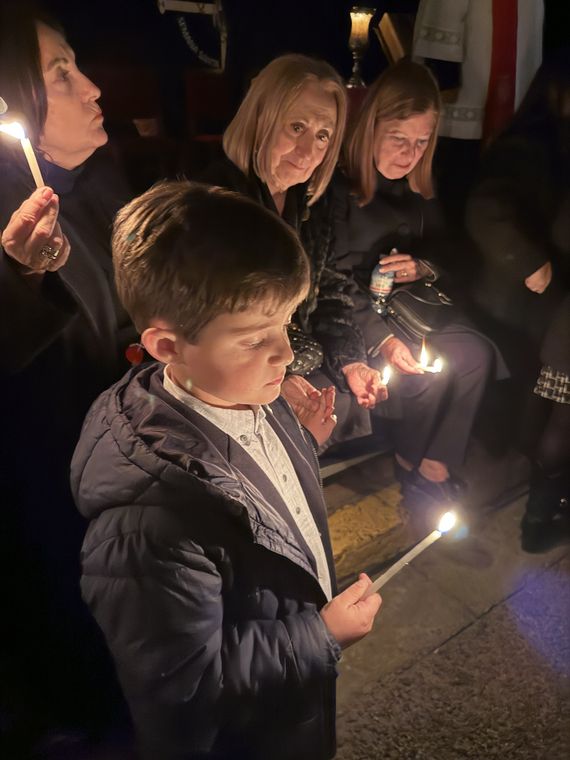 Un niño y varias mujeres sostienen velas encendidas esperando el paso de la procesión