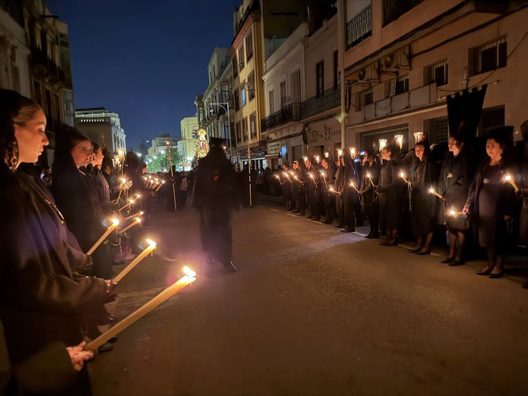 Dos filas de mujeres de negro con velas largas encendidas a ambos lados de la calle